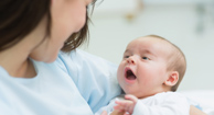Mother holding a baby while he opens his mouth in a hospital room